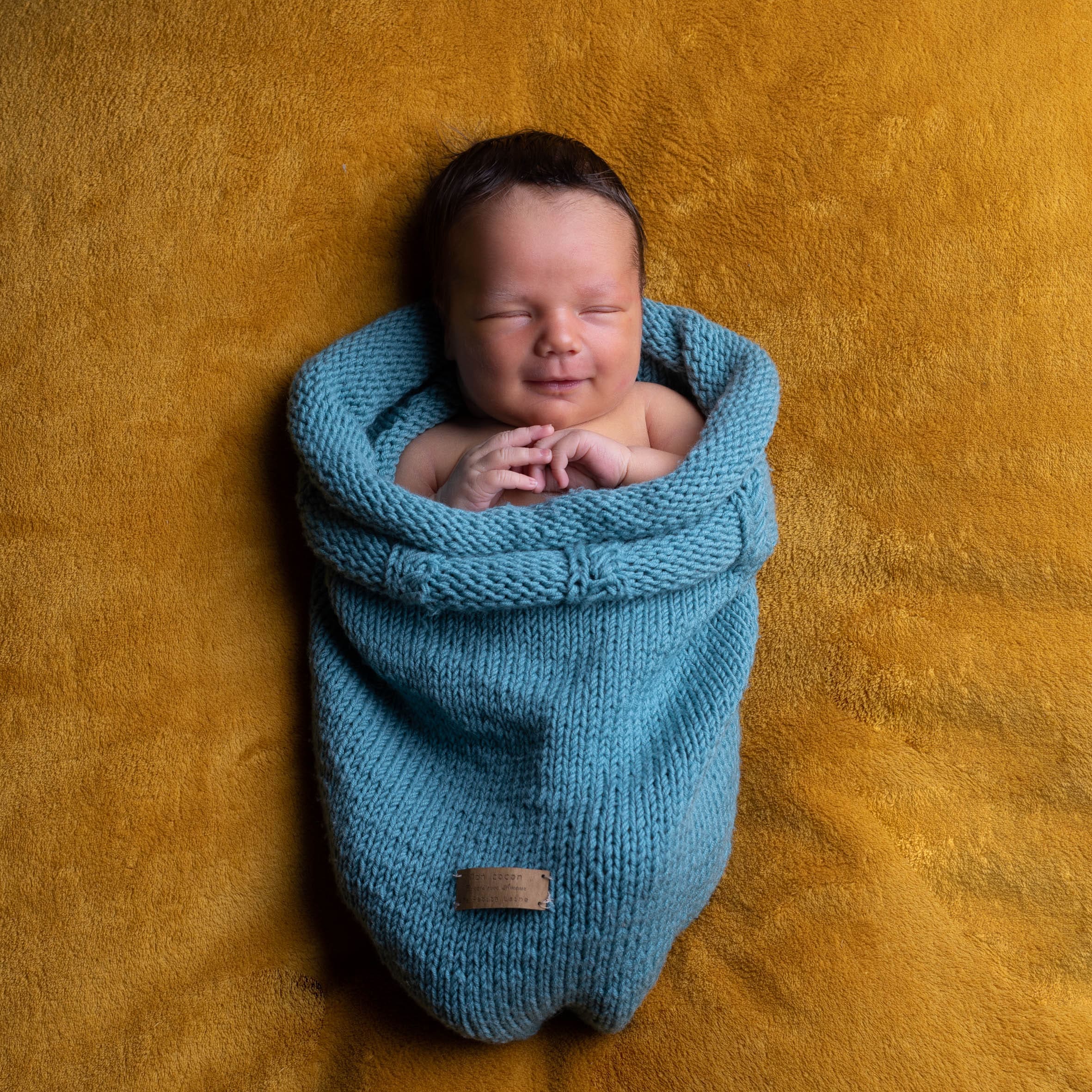 Bébé nouveau-né emmailloté dans un cocon en maille bleu studio Nice