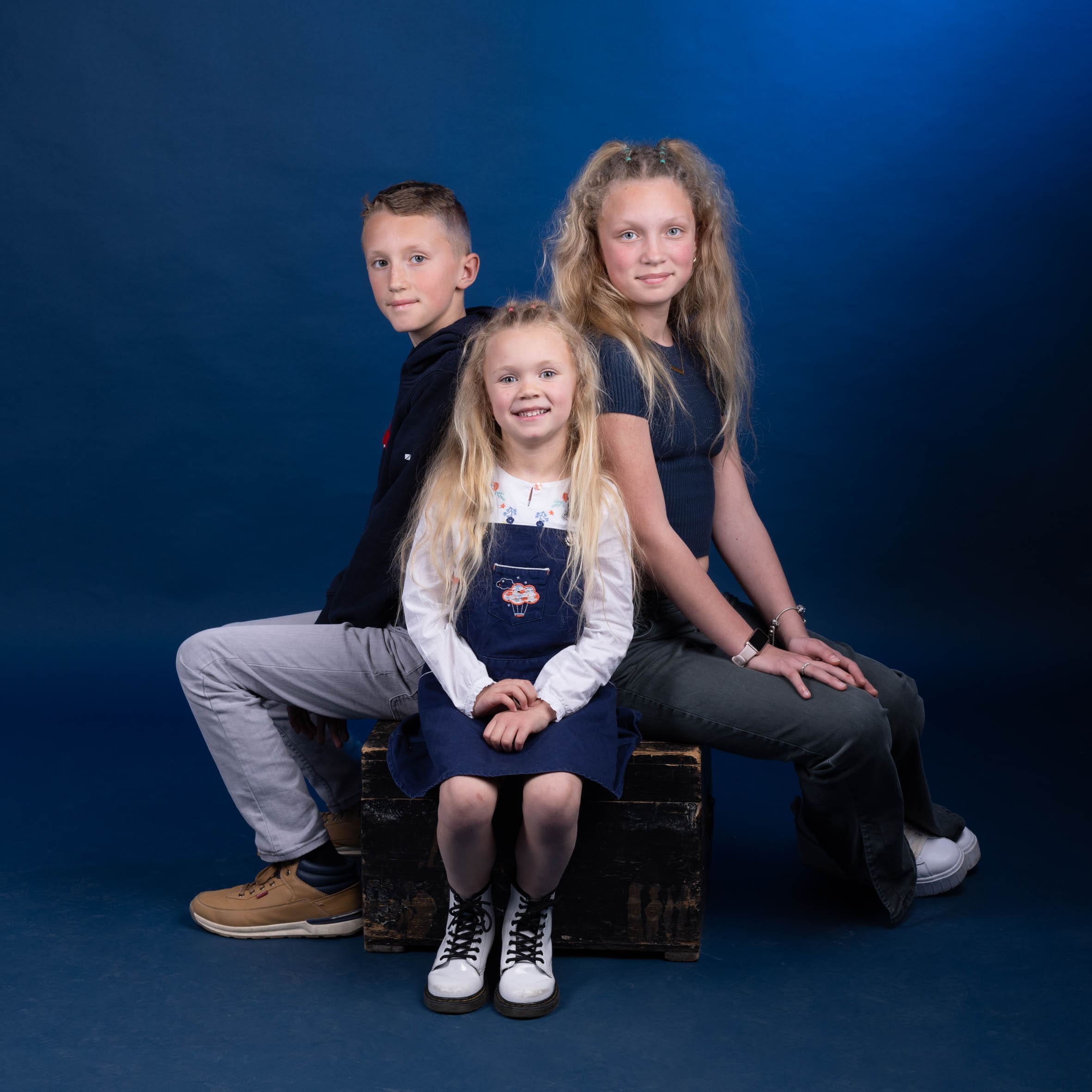 Portrait de fratrie de trois enfants complices sur fond bleu, séance photo studio par Olivia Blanquet à Nice.