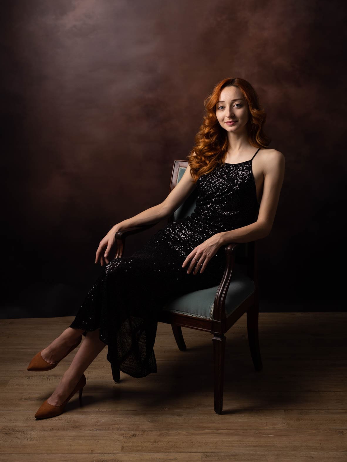 Portrait d'une femme rousse en robe à paillettes noire assise dans un fauteuil, séance estime de soi par Olivia Blanquet à Nice.