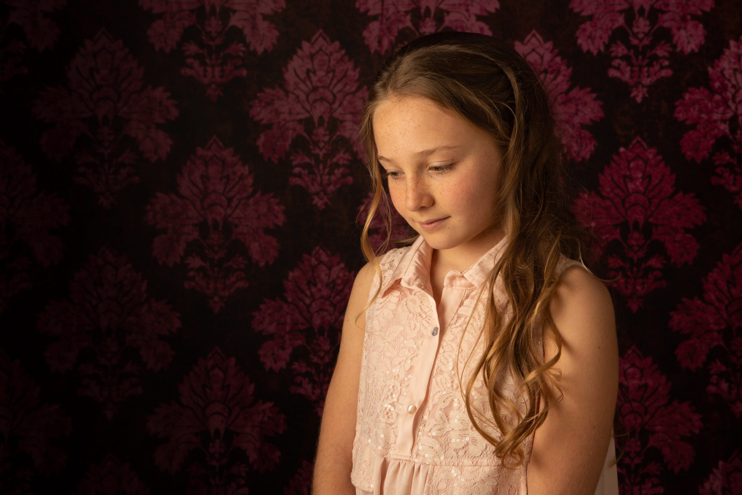 Portrait d'une jeune fille aux cheveux longs devant un fond tapissé bordeaux, par Olivia Blanquet Nice.